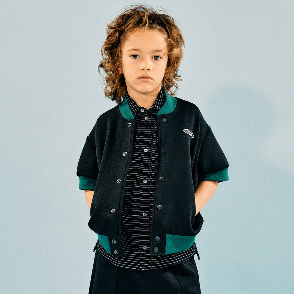 A boy standing against a plain background. He's wearing a cool outfit