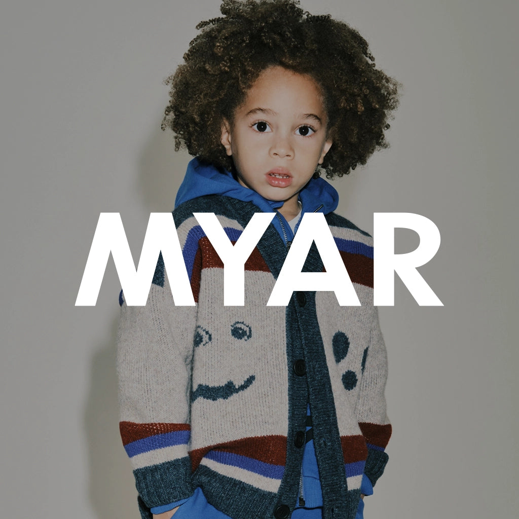 A model with dark curly hair wearing a colored knitwear and a blue tracksuit, set against a solid gray background with a large white 'MYAR' logo.